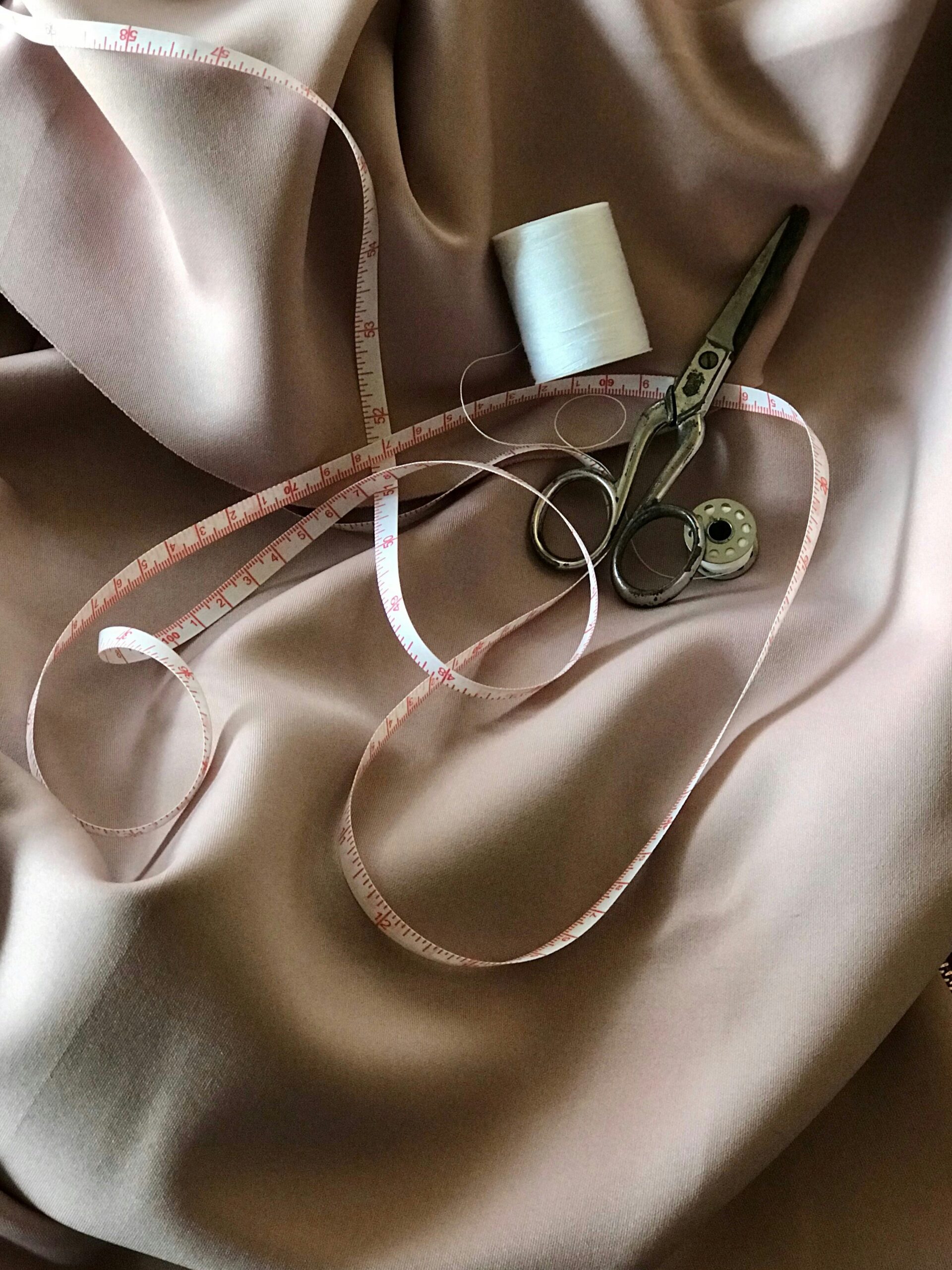 pile of a measuring tape, thread, scissors, and bobbin sitting on top of a pile of fabric
